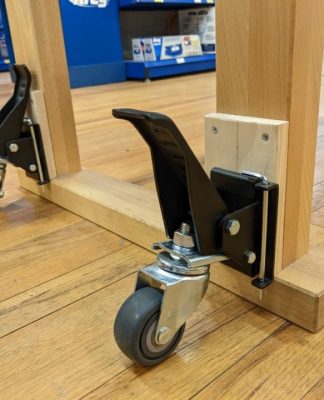 Close-up view of a wooden cart's locking caster wheels on a hardwood floor, providing stability and ease of movement for utility furniture.