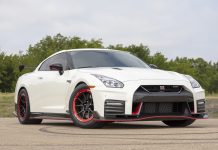 White Nissan GT-R Nismo sports car with black and red wheels on a concrete surface with greenery in the background.