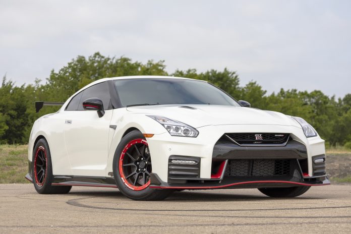 White Nissan GT-R Nismo sports car with black and red wheels on a concrete surface with greenery in the background.