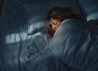 A woman sleeping in bed, wrapped in a blanket with her head resting on a pillow